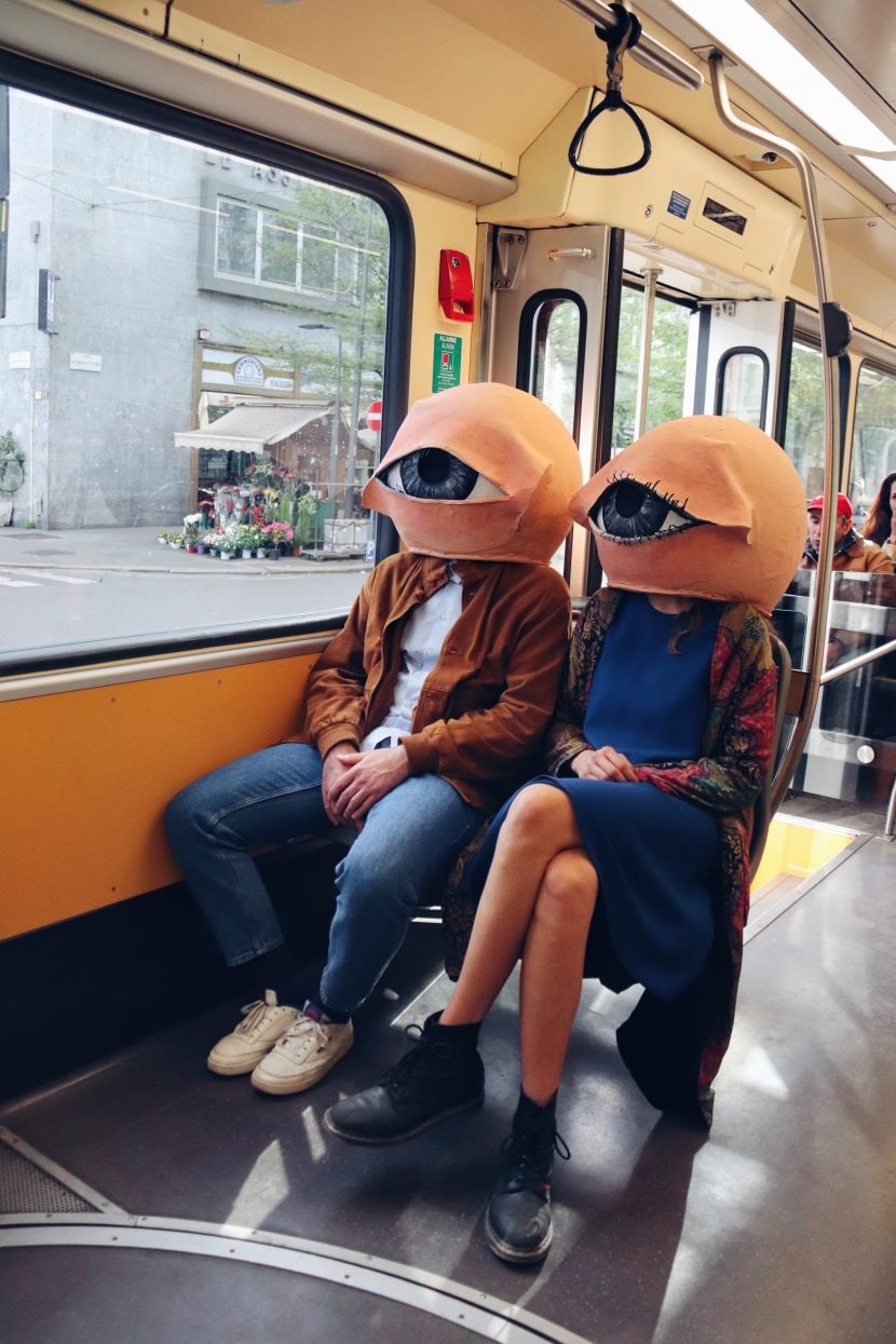 Due ragazzi con in testa la maschera di un grande occhio a Milano.